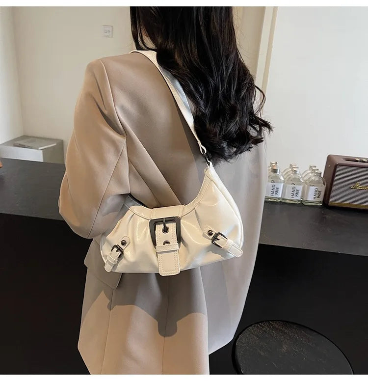 Eine beige Jacke wird von einer Person getragen, die eine weiße Leder-Schultertasche mit Plissee hält.
