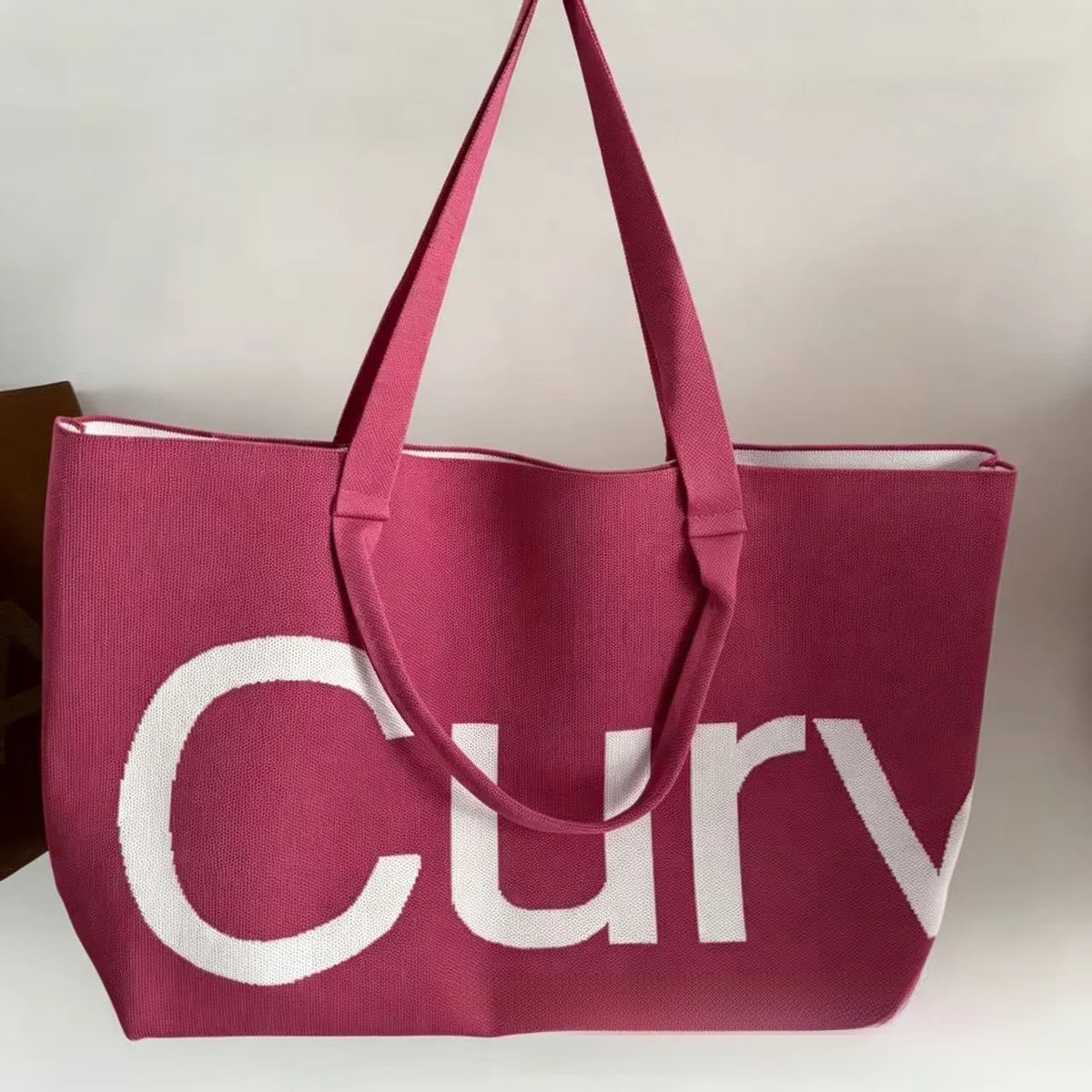 A pink knitted large tote bag with a white strap is shown against a light background.