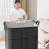 A woman is placing a folded item into a large black foldable non-woven storage bag.