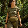 A woman wearing a tactical concealed carry waist pack and olive green shirt walking through a lush forest.