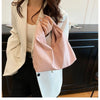 A woman holds a pink leather minimalist crossbody tote bag against a white blazer and black pants.