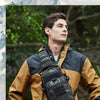 A young man wearing a tan outdoor jacket with a black tactical chest bag on his chest, set against a natural, mountainous bac