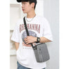 A man wearing a white t-shirt and black hat holds a gray durable waterproof crossbody bag.