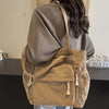 Une personne tient un sac cabas en velours côtelé beige avec plusieurs poches et pompons.
