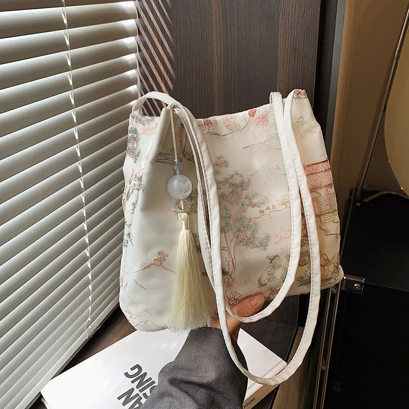 Bolso de hombro de seda jacquard retro color crema con tiras blancas, junto a una persiana.