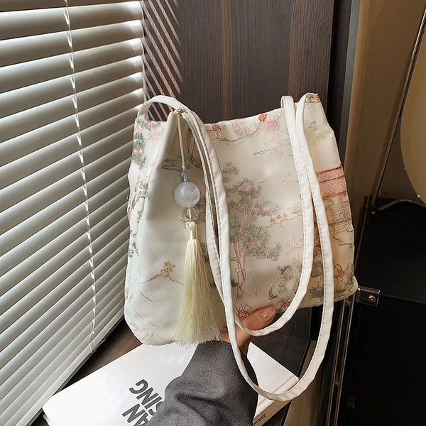A cream colored retro silk jacquard shoulder bag with white straps is displayed next to a window blind.