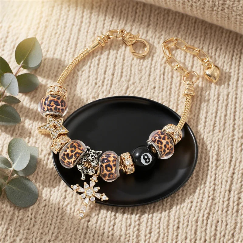 A gold-toned leopard print bracelet featuring black and gold beads and a charm on a dark surface.