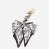 A black and white floral patterned bow made of fabric is attached to a gold chain strap extension for a handbag.