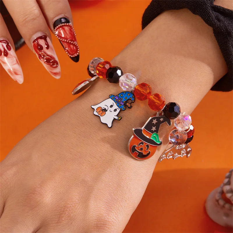 A hand wearing a bracelet made of Halloween pumpkin and ghost charms on an orange background.