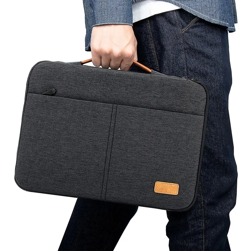 Une housse de protection laptop mince gris foncé tenue par une personne portant un jean foncé.