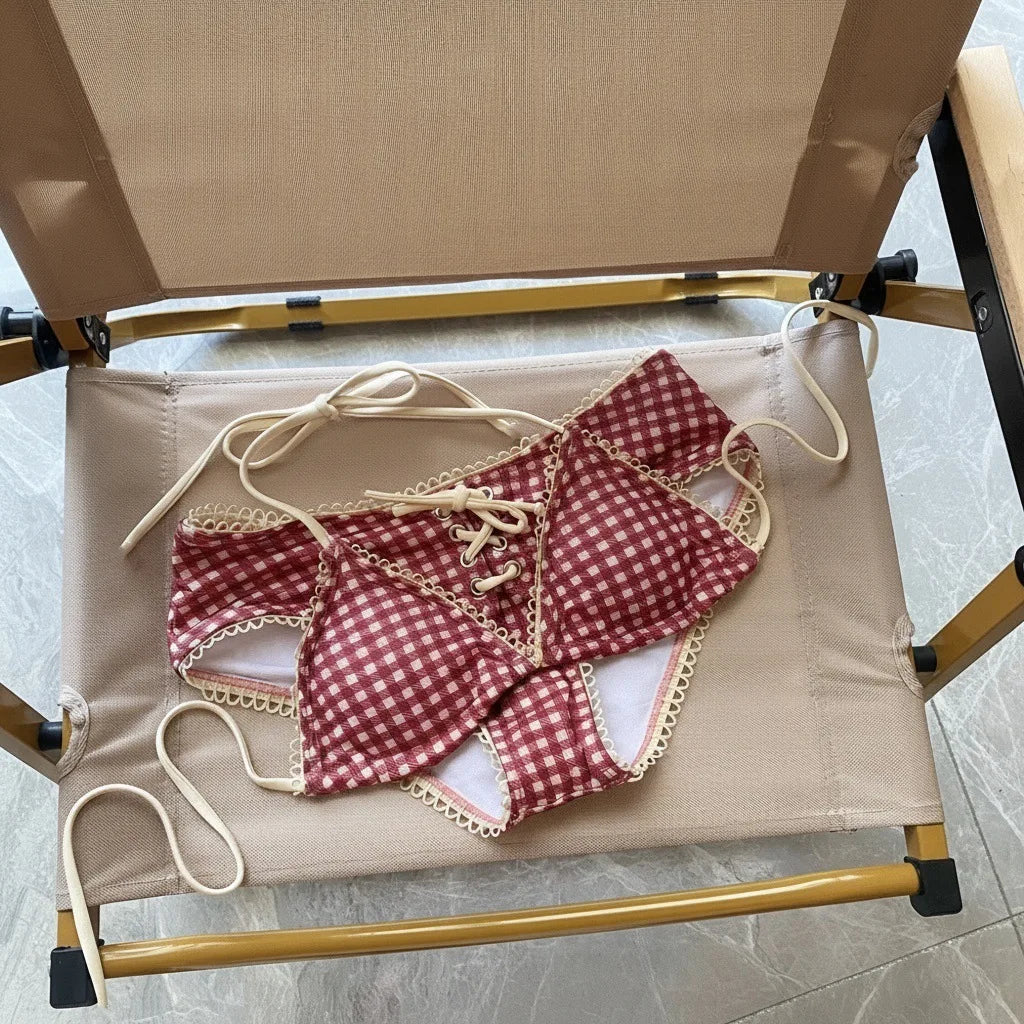 A red plaid bikini set with a halter top and low-rise waist is displayed on a wooden rack.