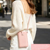 A woman wearing a cream knit sweater and white pants holds a pink PU leather crossbody phone bag.
