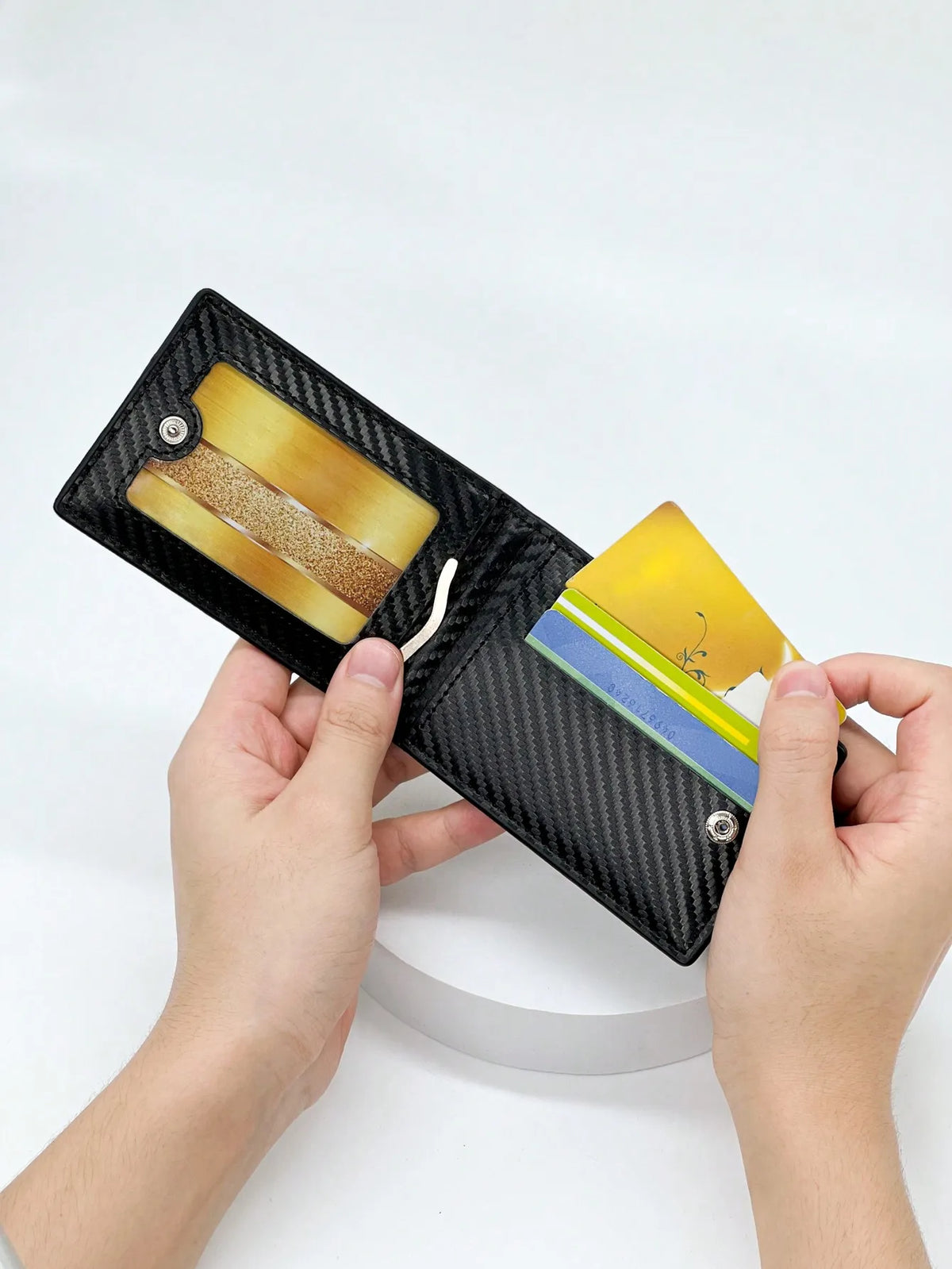 Una mano sostiene una funda para tarjetas de fibra de carbono negra con una tarjeta dorada dentro.