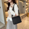 A woman wearing a cream sweater and gray pleated skirt holds a black waterproof nylon crossbody bag.