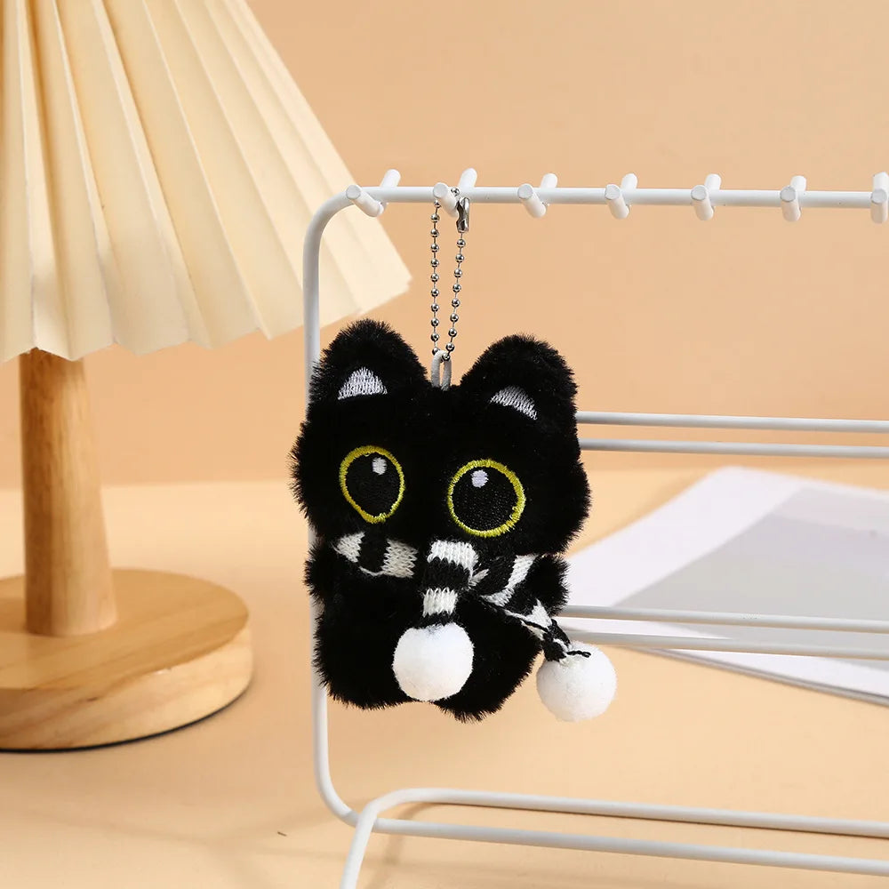 A cute plush black cat keychain charm hanging on a wire rack.