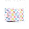 A colorful checkered cosmetic storage pouch featuring pink, yellow, blue, and white squares with pink tassels.