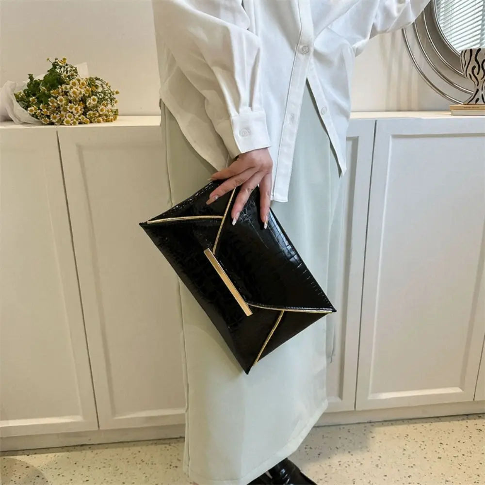 A person wearing a white shirt holds a black crocodile pattern coin purse clutch in front of white cabinetry.
