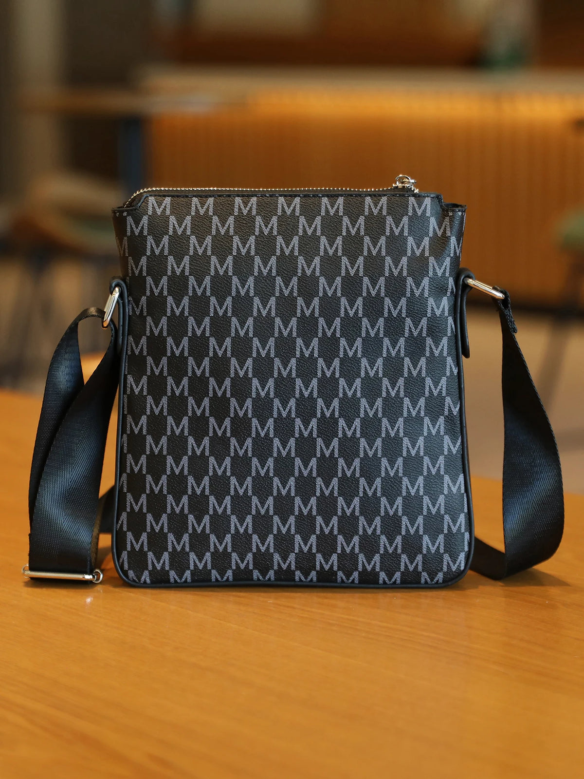 A black men's lightweight crossbody sling bag with a textured monogram pattern resting on a wooden surface.