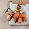 A brown PU leather puppy charm with a bow tie hanging from a light blue denim fabric bag.