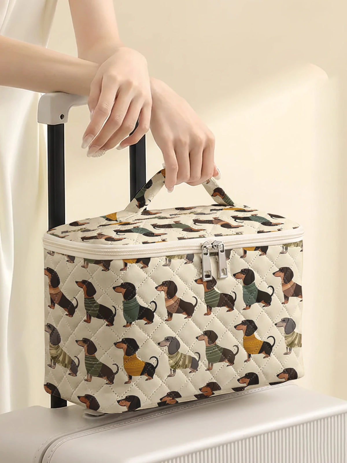 A quilted cosmetic travel bag featuring a dachshund print is being held by a person's hand.