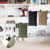 A white pegboard organizer displaying various tools, including a drill, and storage bags on a shelf.