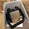 A tan leather digital tablet is resting on a black leather crossbody bag inside a gray upholstered chair.
