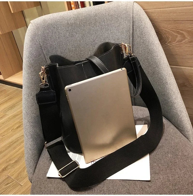 A tan leather digital tablet is resting on a black leather crossbody bag inside a gray upholstered chair.