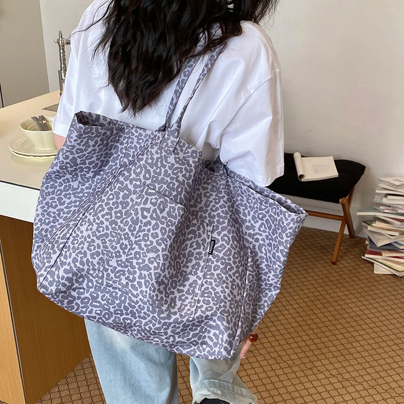 A person holds a gray and white leopard print canvas tote bag against a light background.