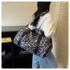 Una mujer lleva una bolsa de viaje de estampado de leopardo con compartimento para zapatos sobre el hombro.