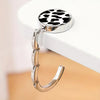 A silver zinc alloy folding handbag hook with a black and white leopard print charm resting on a white surface.