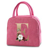 A pink insulated canvas lunch bag featuring a gold letter E and floral accents.