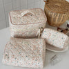 A set of quilted cotton makeup organizers in a floral pattern, including a zippered pouch and a rectangular case.