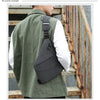 A man wearing a olive green shirt and a dark gray anti-theft crossbody chest bag on his back.