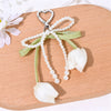 Aesthetic tulip flower bag charm keychain featuring a white petal and pearl strands on a wooden surface.