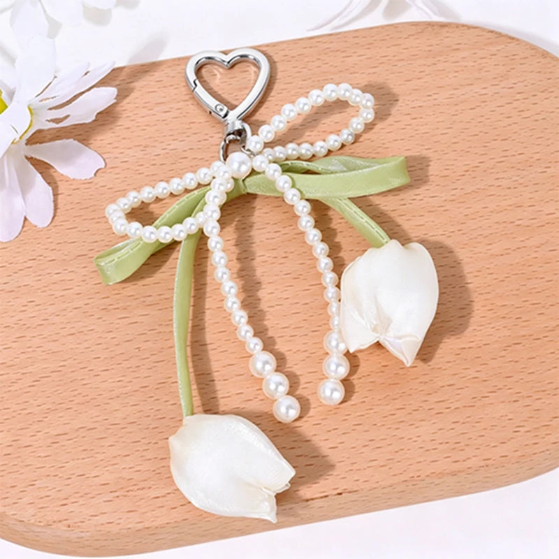 Aesthetic tulip flower bag charm keychain featuring a white petal and pearl strands on a wooden surface.