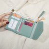 A light mint green PU leather coin clutch wallet with various card slots and a gold tassel is shown against a beige fabric ba