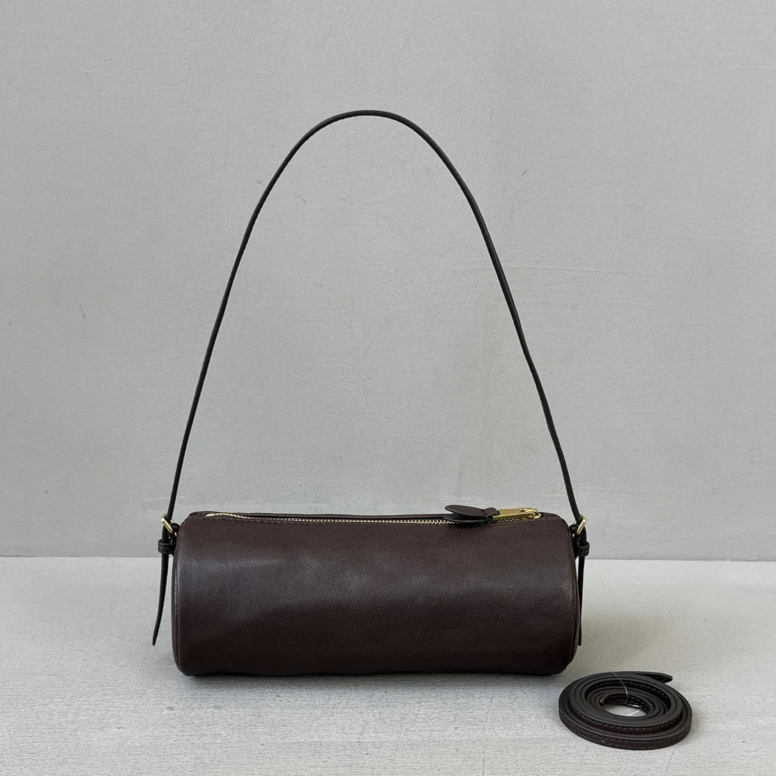 A dark brown vintage cow leather cylinder shoulder bag with a thin black strap is displayed against a light background.