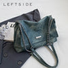 Bolso de cuero verde azulado oscuro con correa de cadena plateada junto a un blazer gris oscuro.