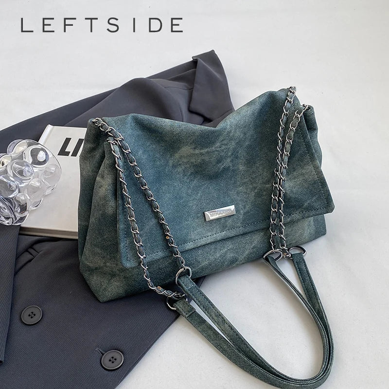 Bolso de cuero verde azulado oscuro con correa de cadena plateada junto a un blazer gris oscuro.