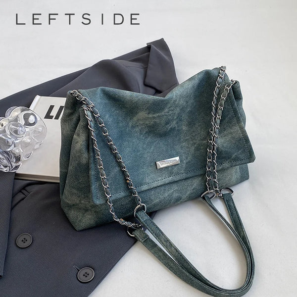 Dunkelteal-Leder-Schultertasche mit silberner Kettenhalskette neben einem dunkelgrauen Blazer