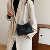 A woman wearing a beige blazer holds a black PU leather chain shoulder bag.