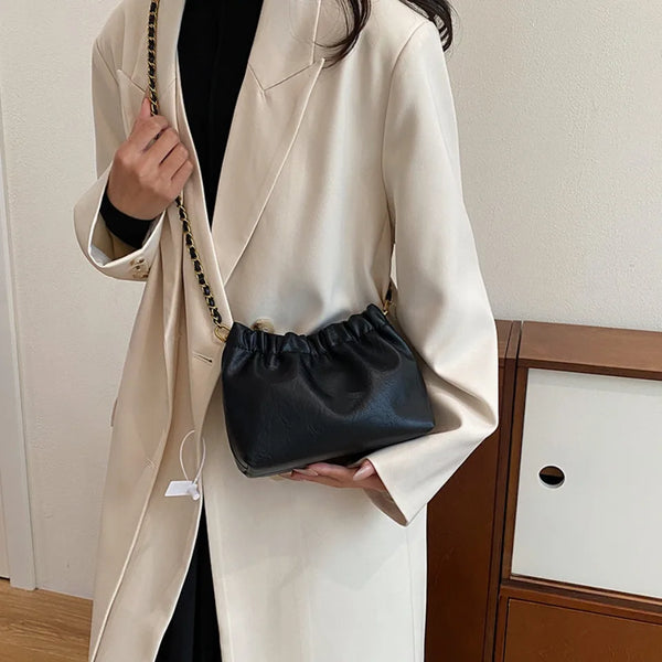 A woman wearing a beige blazer holds a black PU leather chain shoulder bag.