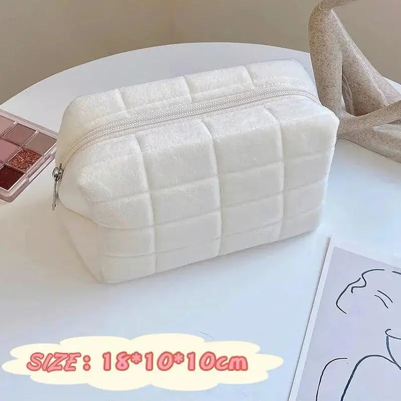 A white quilted zippered cosmetic storage pouch resting on a white surface.