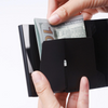 Hands are inserting a ten dollar bill into a black minimalist RFID blocking wallet.