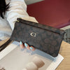 A dark brown patterned zippered wallet resting on a light wooden surface next to some paper.