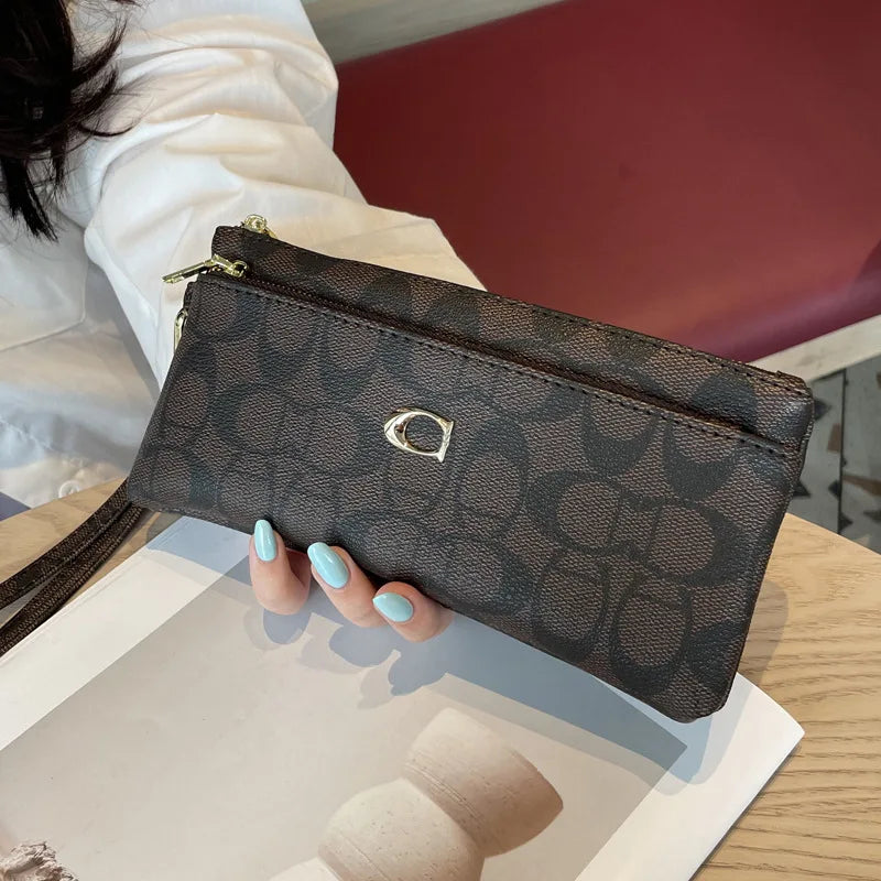 A dark brown patterned zippered wallet resting on a light wooden surface next to some paper.