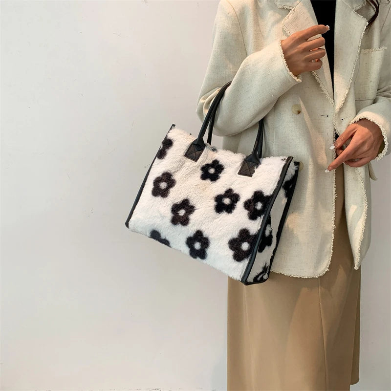 A woman holds a black and white leopard print faux fur designer shoulder tote bag against a white background.