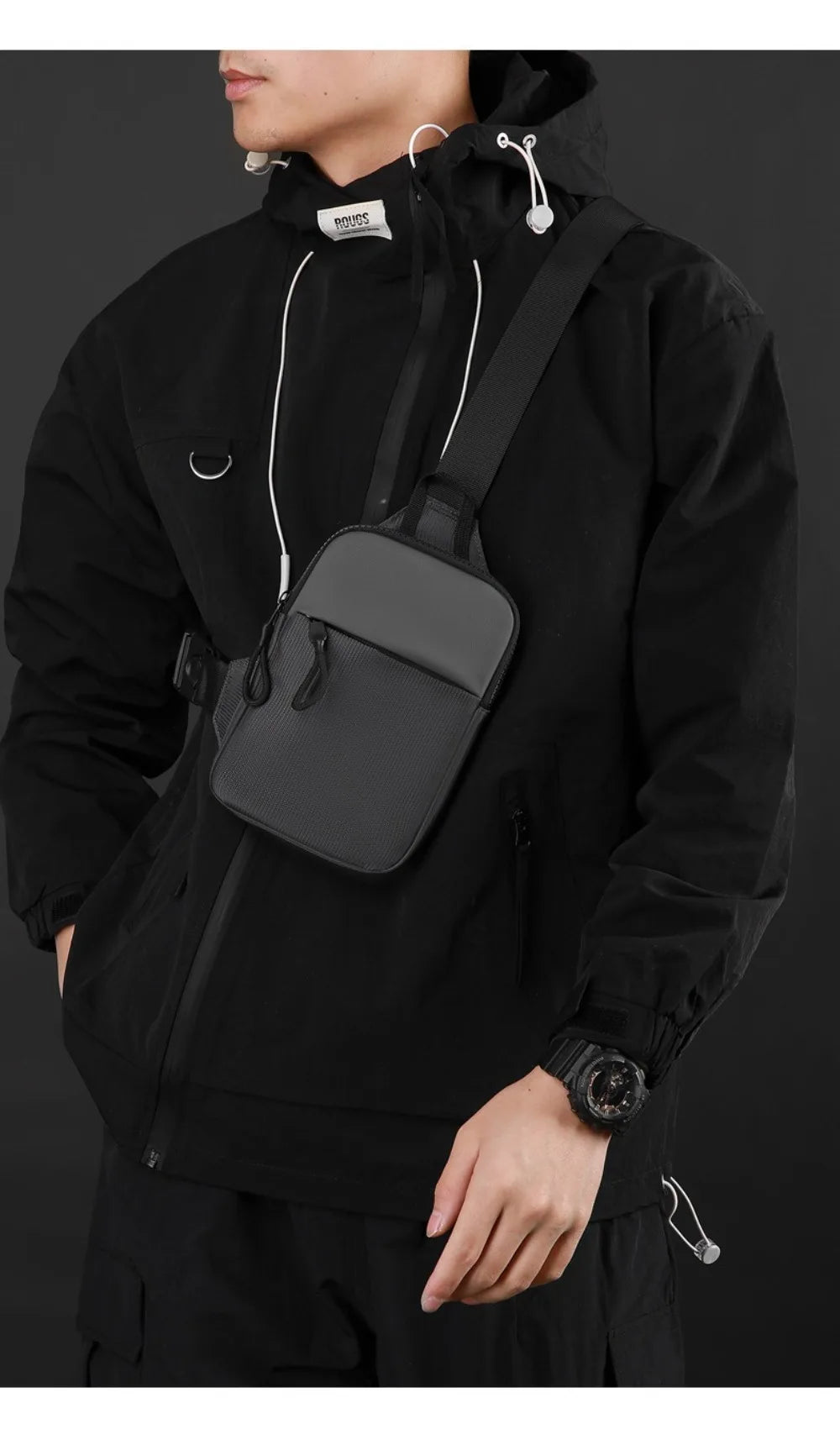 A man wearing a black jacket is holding an olive green Oxford chest bag with a strap.