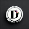 A silver, round letter D with a floral design is shown on a dark background.