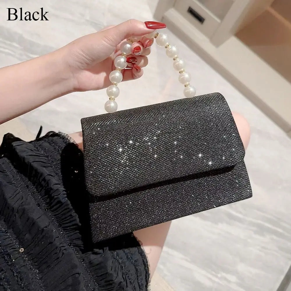 Una mano sostiene un bolso de mano negro con lazo brillante y detalles de perlas.